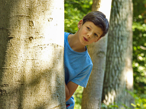 Kind schaut hinter einem Baum hervor