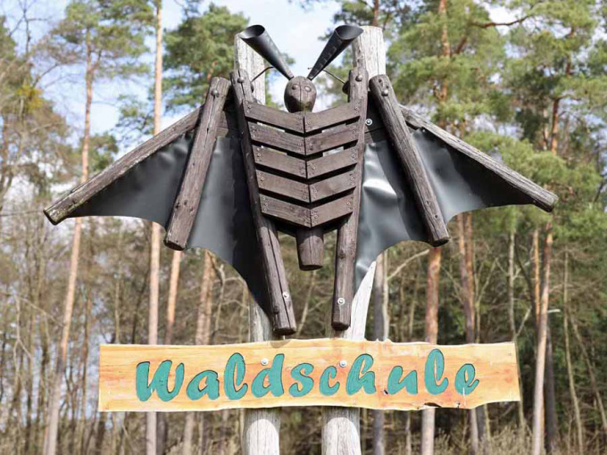 Hinweissschild Waldschule mit Fledermausskulptur