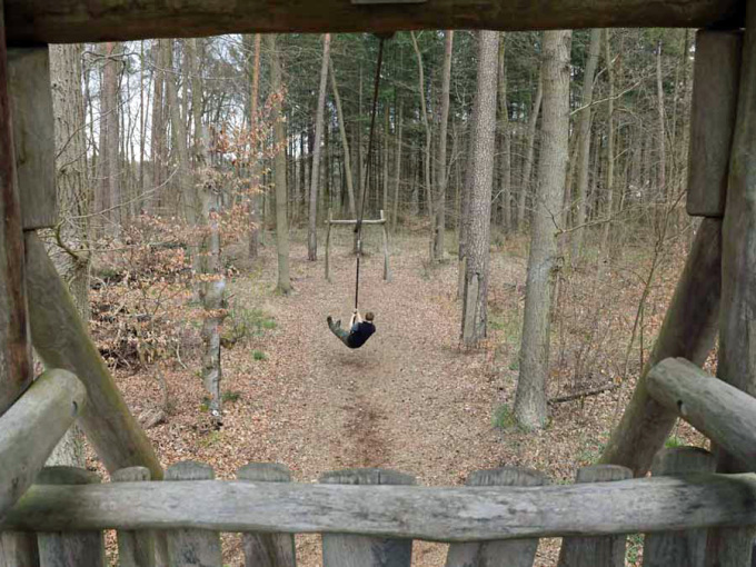 von einem hölzernen Turm aus fährt jemand mit der Seilbahn durch den Wald