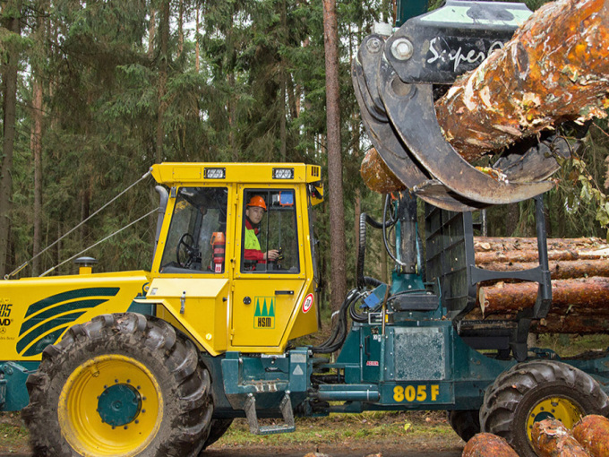 Auszubildener bedient einen Rückeschlepper und hebt Holzstämme auf die Maschine