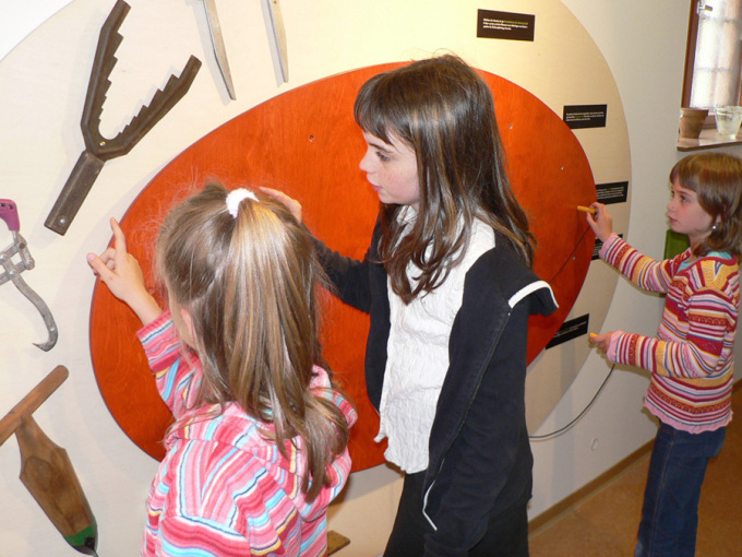 Kinder stehen an einer Tafel mit Forstgeräten 