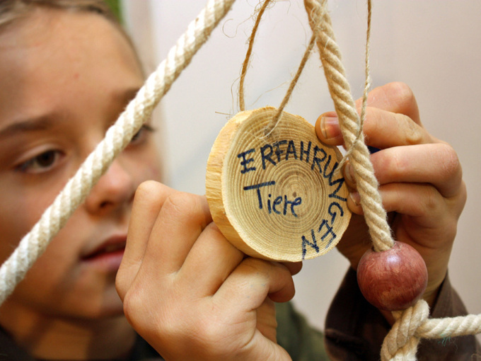 ein Mädchen beschriftet eine Holzplakette des Waldtraumfängers